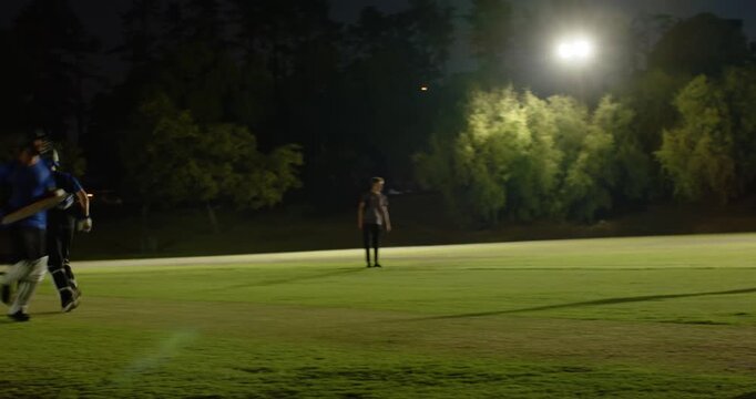 Male cricketers walking to crease and reacting to bowler run-up during floodlit training