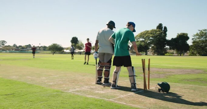 Male batting partners adjusting stumps at park with ball returning preparing next delivery