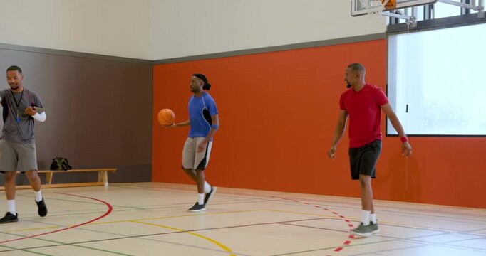 Diverse players practicing basketball on gymnasium court, with basketballs, sports bag and towel