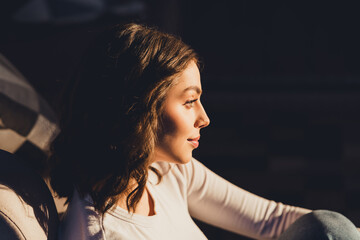 Young woman in warm sunlight looking thoughtful in profile, casual portrait with soft side lighting and relaxed indoor atmosphere © deagreez