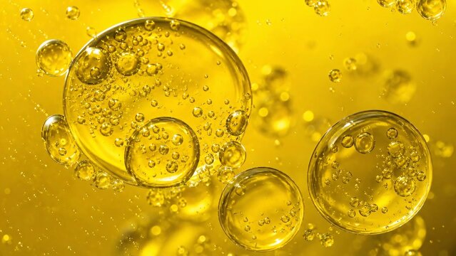 Close up of yellow oil bubbles and small emulsions floating in a yellow liquid.