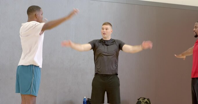 Starting warm-up, diverse male friends performing lateral raises at gym, rotating arms overhead