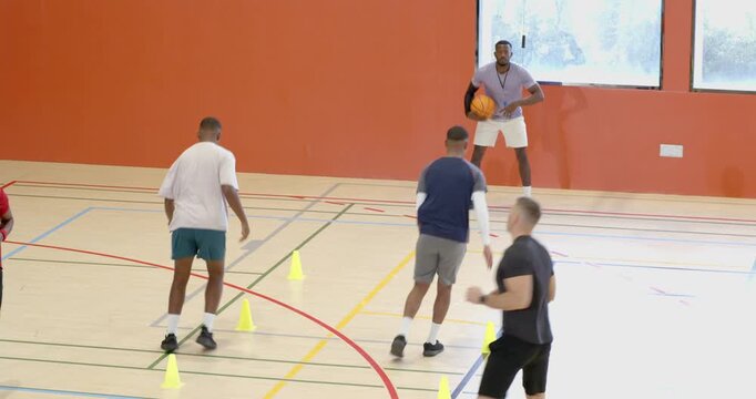 Diverse male players on coach's signal dribbling basketballs through cones on court for training