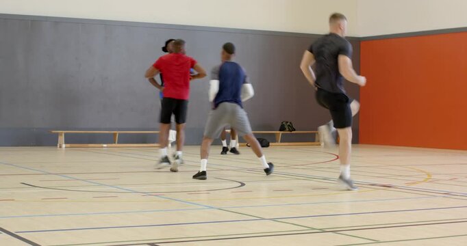 African american trainer leading male players in high-knee warm-up drills with whistle on court