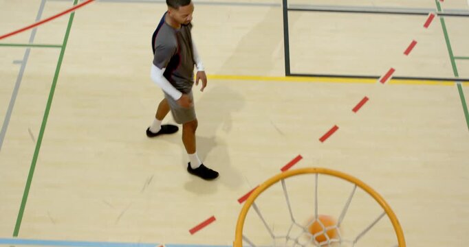 Diverse male team dribbling dunking ball into hoop rebounding trapping dribbler on gym court