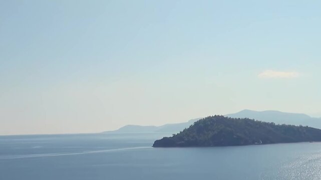 Serene Mediterranean vista unfolds with crystal clear waters. Sunlight dances on surface around lush, green islands, framed by graceful silhouettes of distant mountains under calm morning sky.