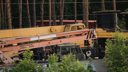 Zdjęcie przedstawia duży żółty dźwig samojezdny zaparkowany w pobliżu gęstego lasu. Na pierwszym planie widoczne są elementy wysięgnika oraz kabina kierowcy maszyny budowlanej. © tomo81