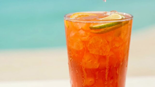 Refreshing cocktail with ice and lime slices, set against a beach backdrop on a sunny day