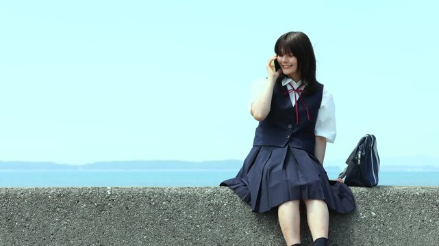 海辺でスマートフォンを使って通話する女子高校生