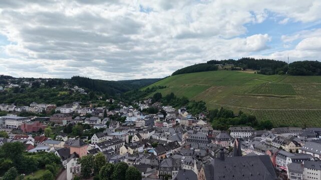 Drone panorama of Saarburg historic old town in Saarland, Germany. Traditional architecture, St. Laurentius Church and surrounding vineyards create a picturesque landscape beneath dramatic summer clou