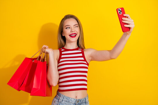 Happy woman taking a selfie with shopping bags on a bright yellow background celebrating shopping and enjoyment
