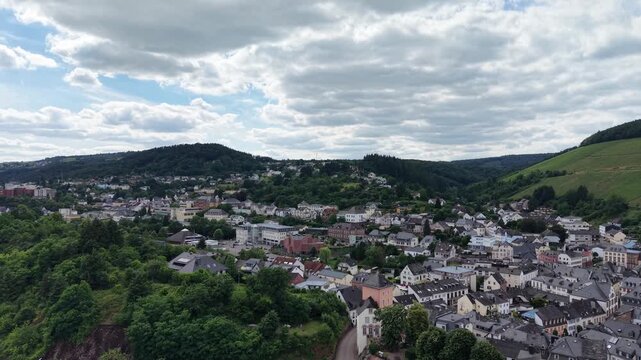 Drone panorama of Saarburg historic old town in Saarland, Germany. Traditional architecture, St. Laurentius Church and surrounding vineyards create a picturesque landscape beneath dramatic summer clou