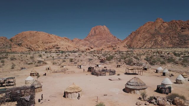Aerial view of a traditional himba village with huts and people walking near spitzkoppe mountain in namibia, africa