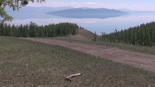 A picturesque overview of Mountain Lake Khuvsgul in Mongolia. Gentle slopes adorned with green grass and larch trees lead down to the vast, calm waters.