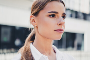 Fototapeta premium Confident young professional woman portrait outdoors looking thoughtful with ponytail, natural makeup and ear piercings