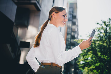 Obraz premium Smiling businesswoman using smartphone outdoors in an urban setting, confident professional checking her phone on a sunny city street for work and lifestyle