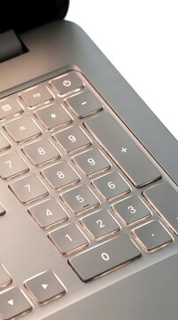 Close-up of illuminated laptop keyboard with numeric keypad, showing backlit keys on metallic device for computing, typing, and data entry work.