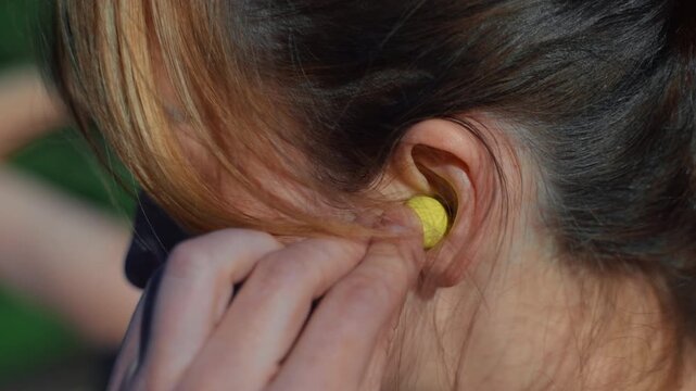 Close-up of a young woman inserting bright yellow wireless earbuds to listen to music for a workout
