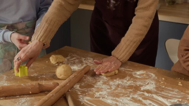 Cropped shot of senior woman and children shaping dough and using cookie cutter at kitchen table. Footage is ideal for family cooking, holiday baking, and intergenerational bonding advertisements