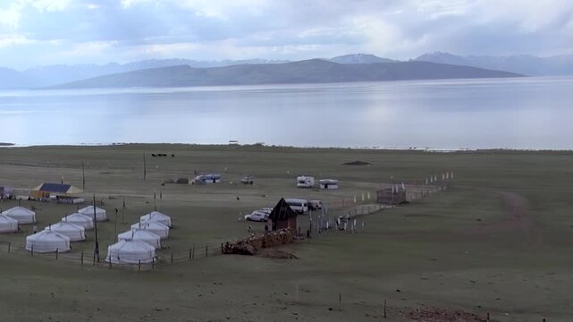 Discover the tranquil allure of Lake Hovsgol in Mongolia. A traditional ger camp graces its emerald shores, offering a peaceful escape amidst rolling hills and distant peaks on a soft, overcast day.