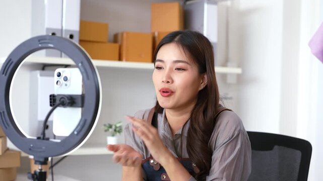 Asian beautiful female bloggers  recording streaming video clip online selling clothes using lighting, cell phone, in studio