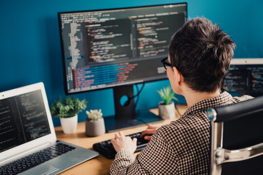 Programmer working at dual-monitor coding workstation with laptop and plants, focused software developer in a home office