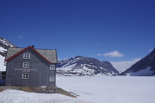 Mountain hut in a snow-covered late winter landscape, surrounded by mountains and a frozen lake, under a clear blue sky, Langevatn, Geiranger, Fjell, Norway