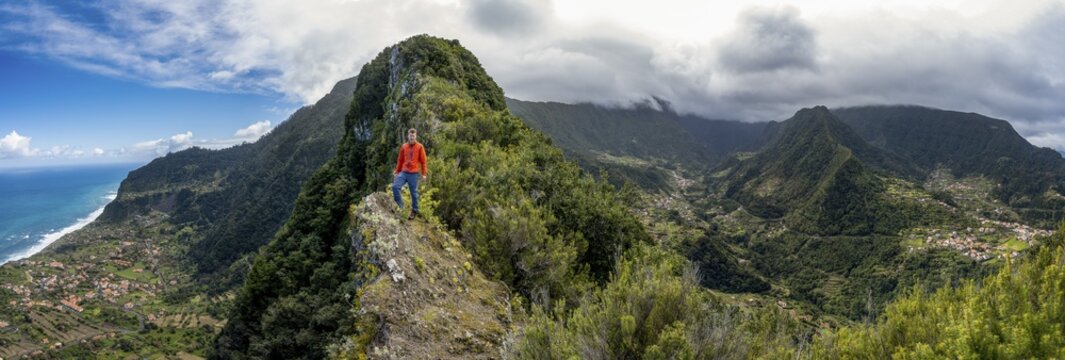 Hikers on the ridge of Pico do Alto, panorama, view of densely overgrown mountains and the village of Boaventura, view of the coast and sea with the village of Arco de Sao Jorge, Madeira, Portugal