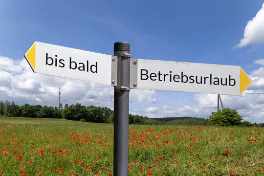 Wanderschild mit der Aufschrift BETRIEBSURLAUB und BIS BALD vor einer Wiese mit Mohnblumen