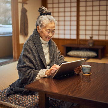 Japanese senior woman using tablet at kotatsu in winter