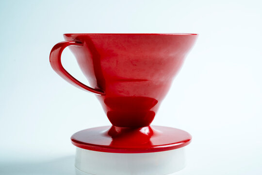 A close-up shot of a bright red ceramic pour-over coffee dripper cone with a handle, sitting on a white background, perfect for manual filter brewing