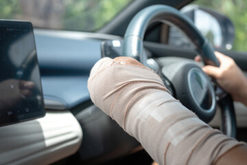 Close-up at car driver's left hand wrapped in an elastic medical bandage gripping a car steering wheel. Land transportation accident concept. © Nattawit
