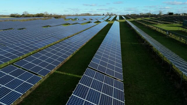 High angle drone tracking shot of a large scale ground mounted solar array in the British countryside