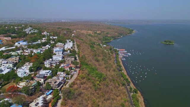Drone footage moving forward along the shoreline of Upper Lake in Bhopal featuring Boat Club boating facilities, Van Vihar National Park landscape, and scenic waterfront views under clear daylight.