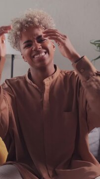 An excited young African American woman plays a video game with a gamepad, reactively losing the match, showing intense disappointment, and covering her face with her hands.