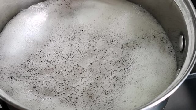 Boiling water with foam and bubbles in stainless steel cooking pot