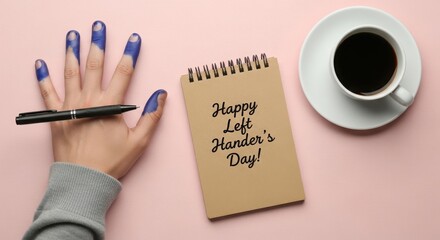 Left hand with blue ink stained fingertips holding a pen next to a notepad and coffee cup