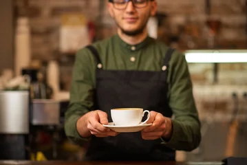 A smiling male barista holding and serving a white cup of hot coffee © Nomad_Soul