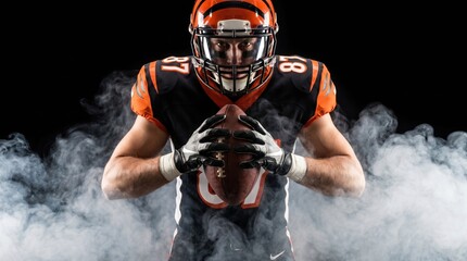 Obraz premium American football player on a dark background in smoke in black and orange equipment.