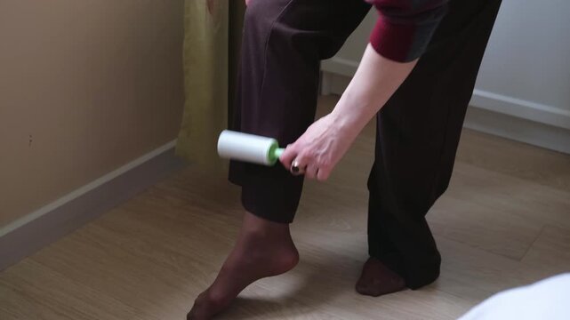 woman uses sticky lint roller for cleaning trousers from pet hair. effective lint roller keeps clothes neat and tidy. daily clothing care with lint roller ensures perfect professional look.