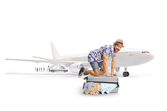 Cheerful man trying to close an overpacked suitcse next to a plane