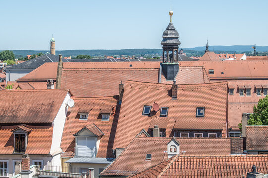 Aussicht auf D&auml;chermeer der b&uuml;rgerlichen Bergstadt in Bamberg mit Haus mit eingesunkenem Dachfirst und Kirchturm der Kirche Elisabeth im Sand im harten Mittagslicht vor blauem Himmel.