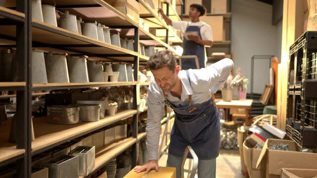 Warehouse worker experiencing back pain from lifting heavy boxes, highlighting workplace risk and physical strain
