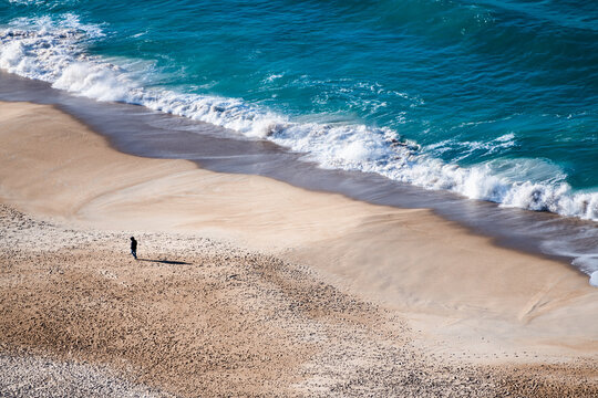Big ocean waves breaking on the beach. Atlantic ocean coast in Nazare, Portugal. Man walking on the beach.