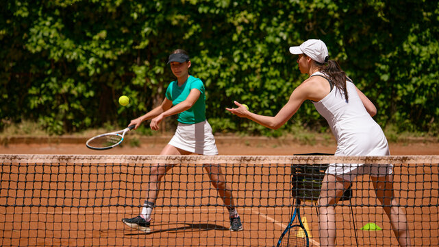 Coach feeds tennis ball to teenage girl during net drill on clay court. Concept of tennis coaching, teen sport, reaction training, academy lesson and fitness.
