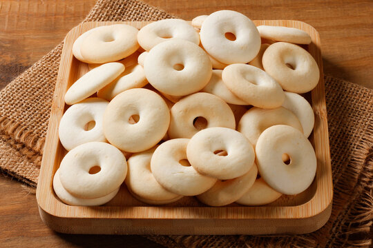 Traditional Brazilian coconut sequilho cookies arranged in a wooden tray over burlap fabric on a rustic wooden table.