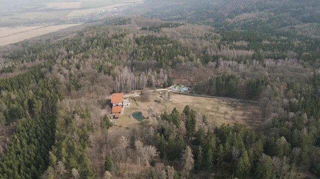 Aerial drone panorama captures the vast mixed forests of the Brdy highlands near Rochota during early spring, showing a blend of evergreen conifers and leafless deciduous trees across rolling hills.