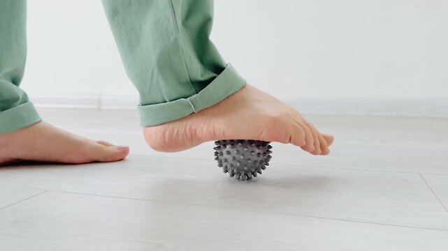 Spiky massage ball pressed by foot on wooden floor in bright indoor setting