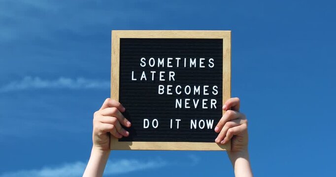 Young female hands holding a letter board with Inspirational motivational quote Sometimes later becomes never. Do it now words against blue sky outdoors