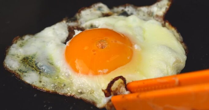 Close up macro view of an overcooked fried egg about to burn inside a hot black skillet pan showing crispy brown charred edges